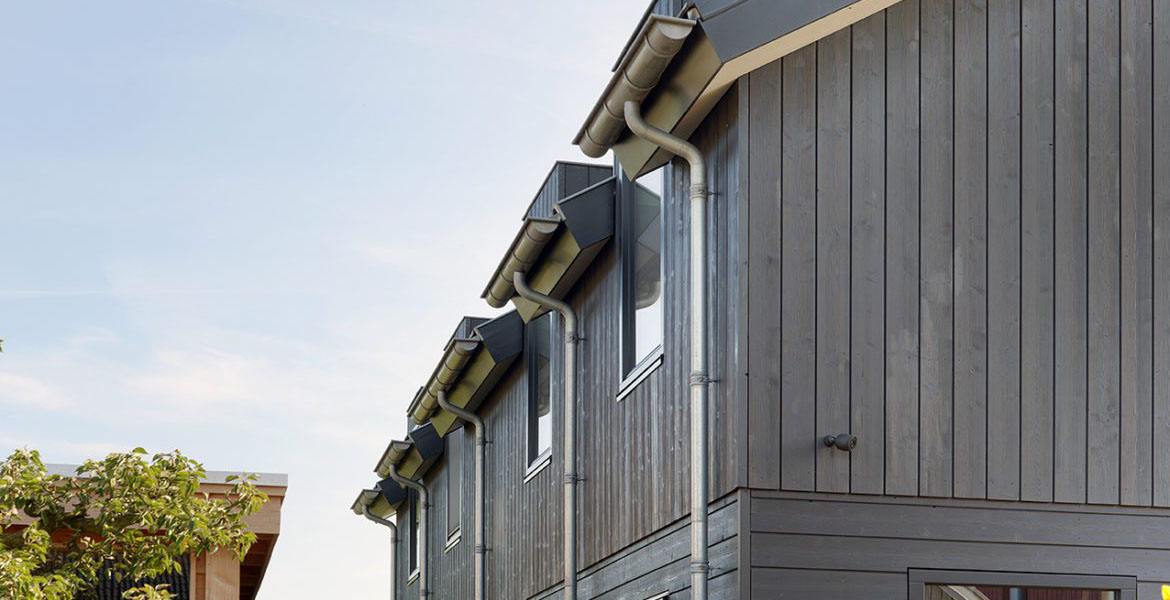 De zijkant van een landelijke woning met zwarte houten panelen en dakgoten. 